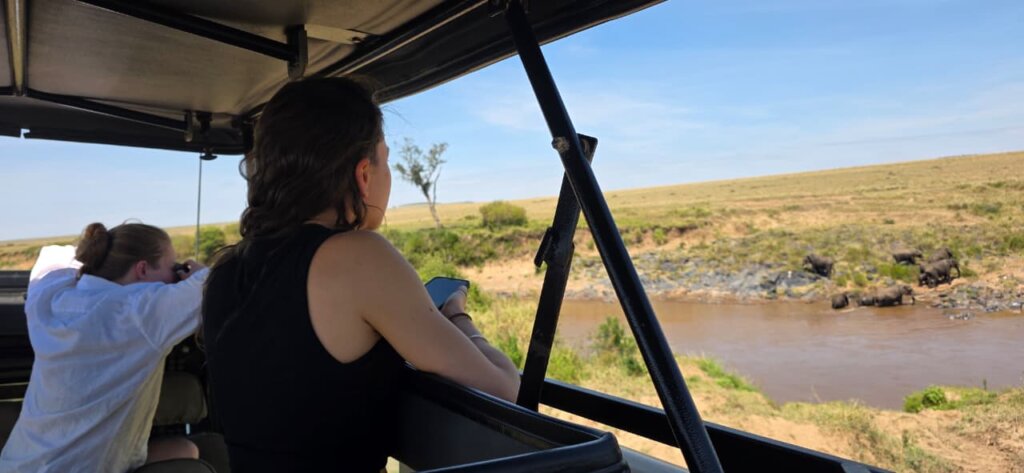 TOURISTS WATCHING IN MASAI MARA USIN THE POP UP ROOF OF 4X4 SAFARI LAND CRUISER