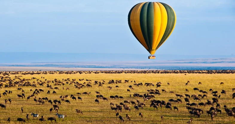 Hot air balloon flying over Maasai Mara at sunrise in luxury experience safari package