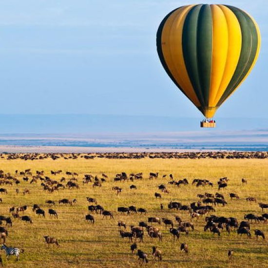 Hot air balloon flying over Maasai Mara at sunrise in luxury experience safari package
